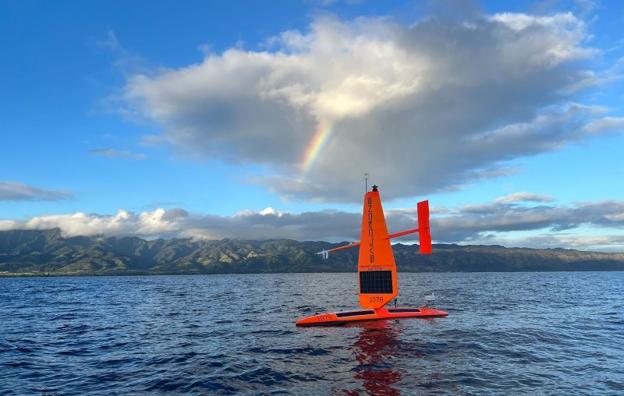 Orange drone in the middle of blue water with clouds above and a rainbow in the background