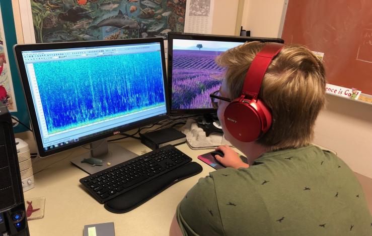 A master's student sitting in front of a computer looking at sound spectrogram on a computer from 