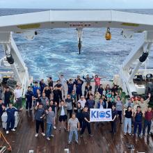 Group photo of 50 participants on the deck of the ship holding a KIOS banner 