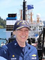 Sarah smiling in blue NOAA Corps uniform with blue hat on in front of a NOAA Ship